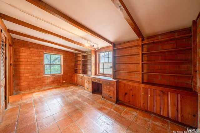 interior space featuring a wealth of natural light, built in desk, lofted ceiling with beams, and brick wall