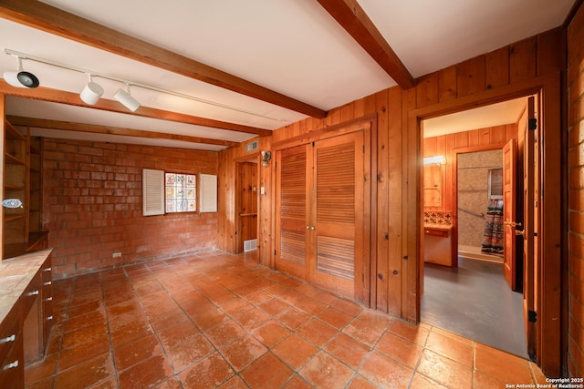 interior space with beamed ceiling, rail lighting, and wooden walls