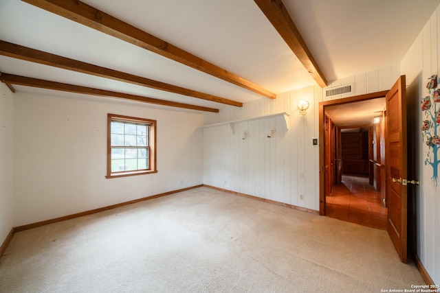 carpeted empty room with beam ceiling and wooden walls