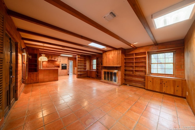 unfurnished living room featuring light tile patterned floors, built in features, a brick fireplace, beamed ceiling, and wood walls