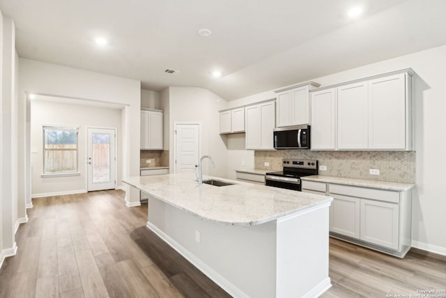 kitchen featuring appliances with stainless steel finishes, sink, a center island with sink, and light stone counters