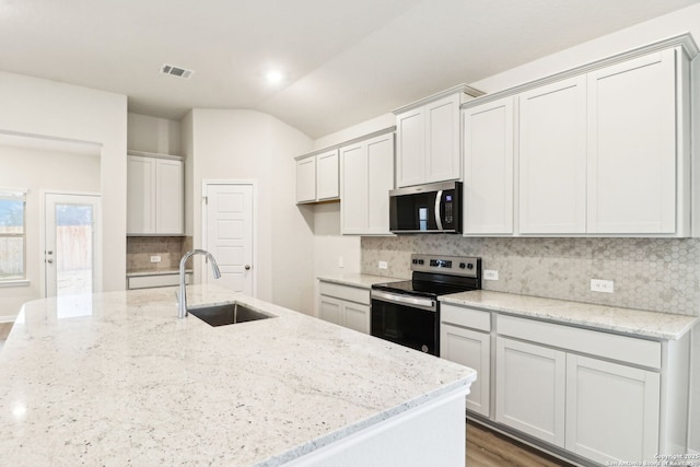 kitchen with appliances with stainless steel finishes, lofted ceiling, sink, decorative backsplash, and light stone countertops