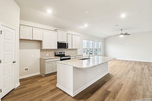 kitchen featuring sink, vaulted ceiling, a center island with sink, stainless steel appliances, and light stone countertops