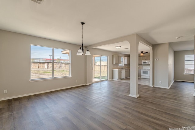 unfurnished living room with dark wood-type flooring and ceiling fan with notable chandelier