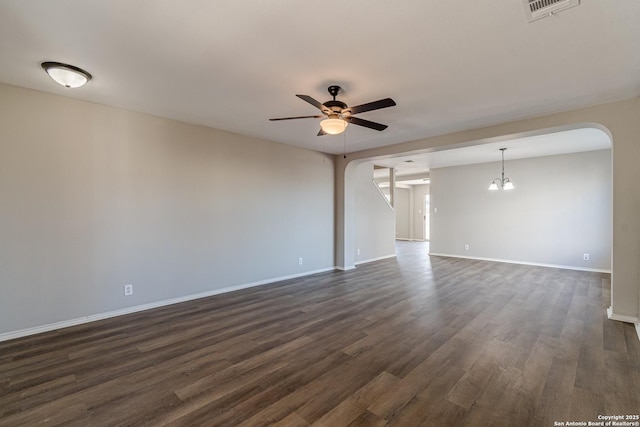 empty room featuring ceiling fan with notable chandelier and dark hardwood / wood-style floors