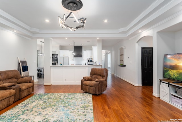 living room with a raised ceiling, a notable chandelier, ornamental molding, and hardwood / wood-style flooring