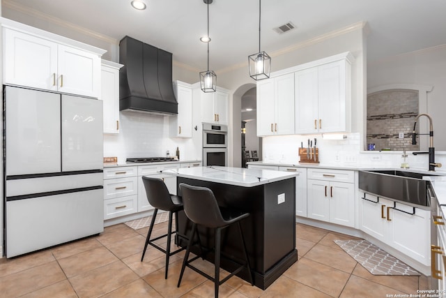 kitchen with backsplash, premium range hood, a kitchen island, white cabinetry, and stainless steel appliances