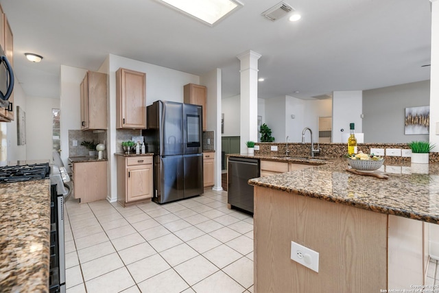 kitchen with dark stone countertops, sink, light brown cabinets, stainless steel appliances, and decorative columns