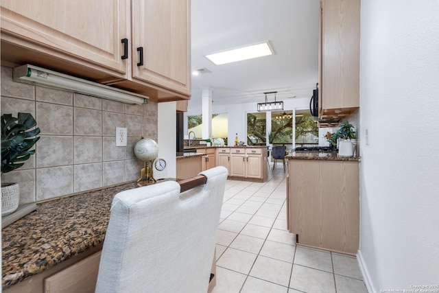 kitchen featuring dark stone counters, light brown cabinetry, backsplash, kitchen peninsula, and light tile patterned floors