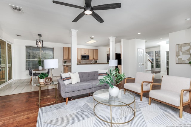 living room featuring light wood-type flooring, ceiling fan, and ornate columns