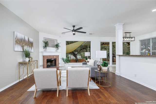 living room with a fireplace, sink, dark hardwood / wood-style flooring, ceiling fan with notable chandelier, and ornate columns