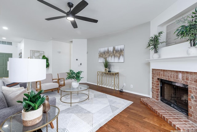 living room with dark wood-type flooring, a brick fireplace, and ceiling fan