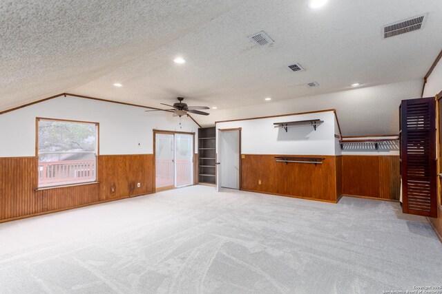 unfurnished living room with ceiling fan, light colored carpet, vaulted ceiling, and a textured ceiling