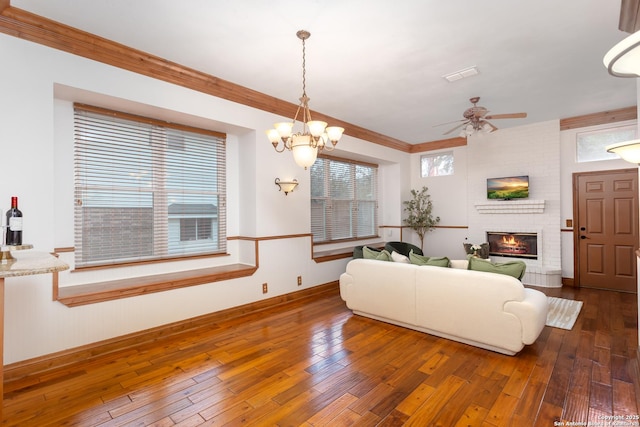 living room featuring a fireplace, dark wood-type flooring, ceiling fan with notable chandelier, and ornamental molding