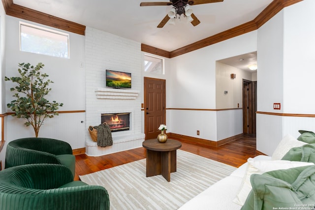 living room with ceiling fan, light wood-type flooring, a fireplace, and ornamental molding