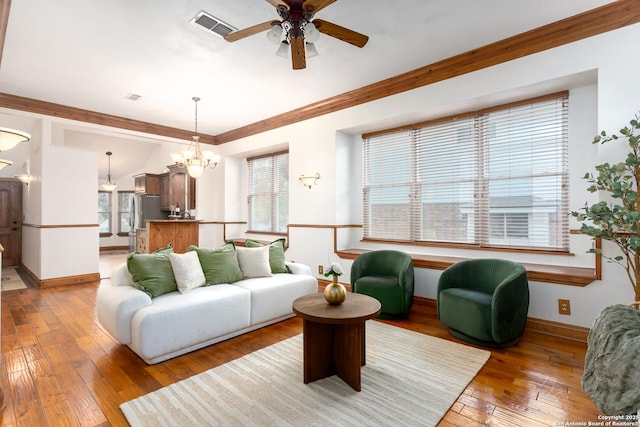 living room featuring hardwood / wood-style flooring, vaulted ceiling, ornamental molding, and ceiling fan with notable chandelier