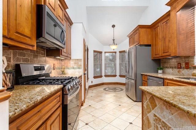 kitchen featuring decorative light fixtures, light stone counters, appliances with stainless steel finishes, and tasteful backsplash