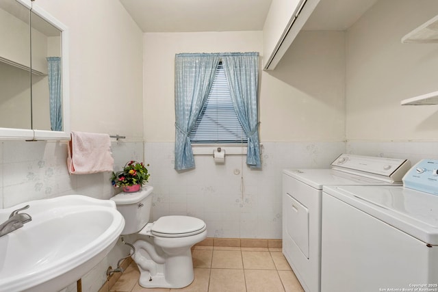 bathroom featuring toilet, tile patterned flooring, tile walls, washing machine and dryer, and sink