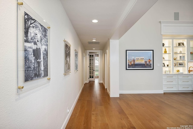 corridor with wood-type flooring and built in shelves