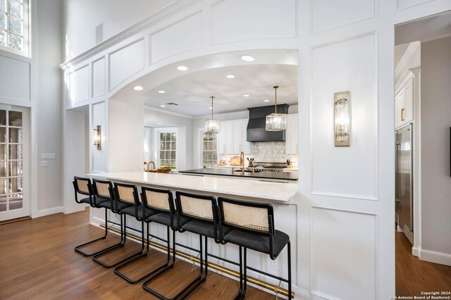 kitchen with a kitchen bar, white cabinetry, a healthy amount of sunlight, premium range hood, and hanging light fixtures