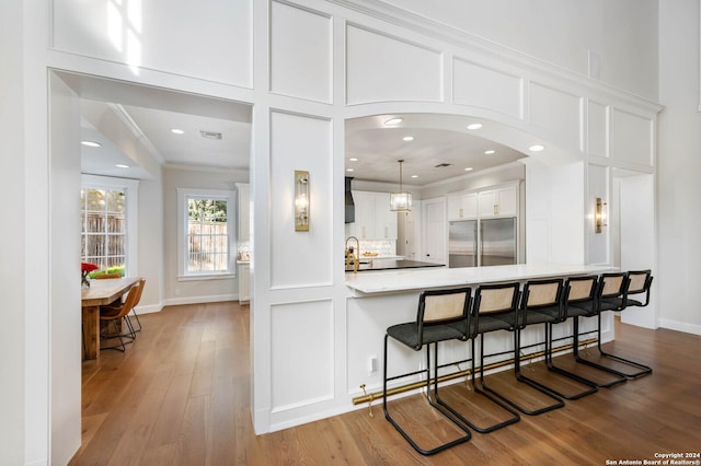 kitchen with kitchen peninsula, built in refrigerator, crown molding, white cabinets, and sink