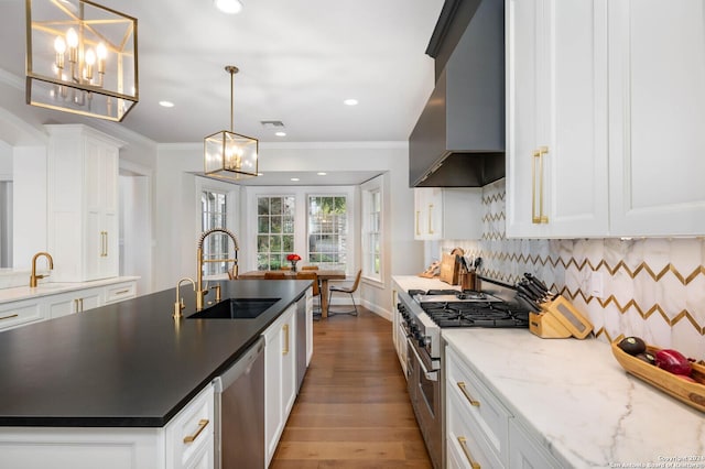 kitchen featuring white cabinets, appliances with stainless steel finishes, wall chimney exhaust hood, sink, and a kitchen island with sink