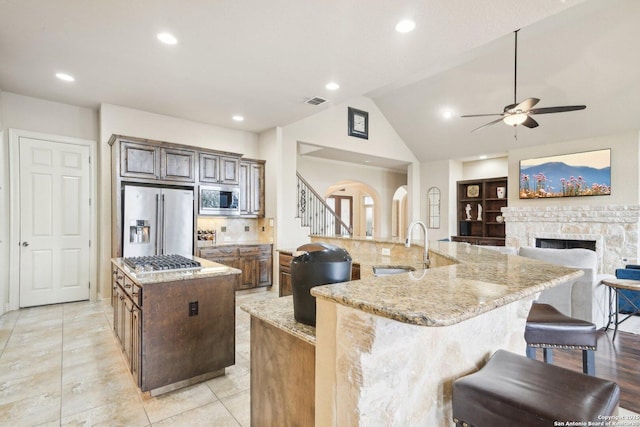 kitchen featuring a brick fireplace, appliances with stainless steel finishes, a breakfast bar area, built in features, and a large island with sink