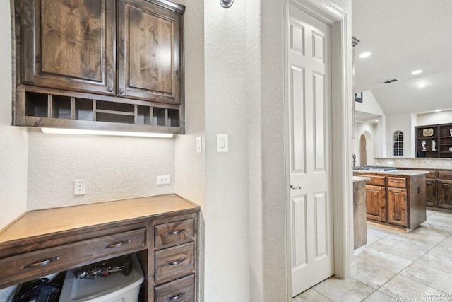 kitchen featuring light tile patterned floors, lofted ceiling, dark brown cabinets, and tasteful backsplash