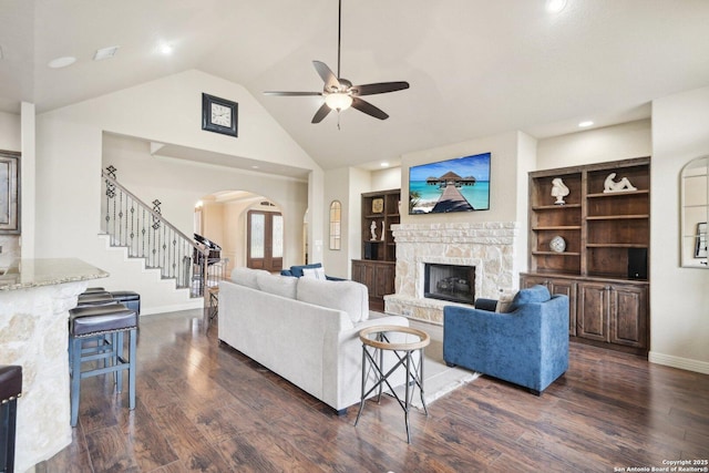 living room featuring built in shelves, dark hardwood / wood-style flooring, and a stone fireplace