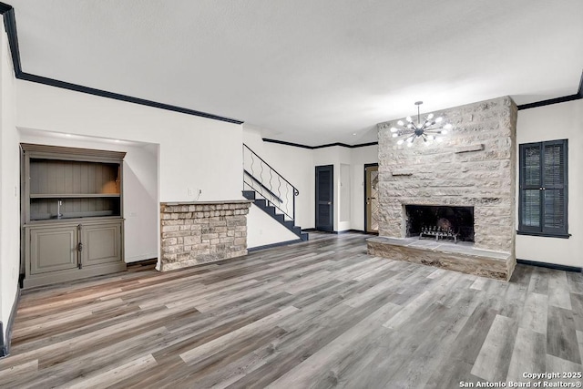 unfurnished living room featuring a chandelier, hardwood / wood-style floors, crown molding, and a stone fireplace