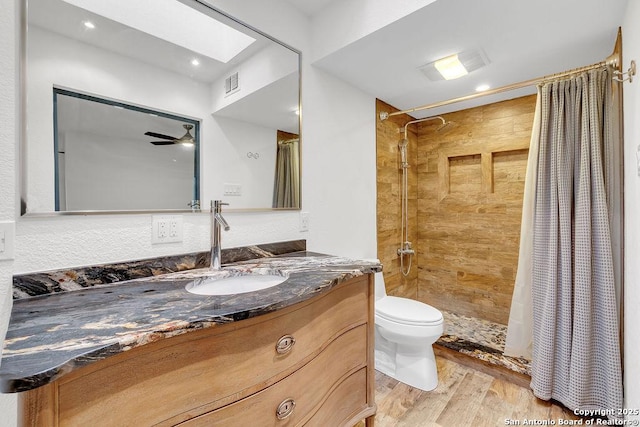 bathroom with ceiling fan, vanity, toilet, wood-type flooring, and a skylight