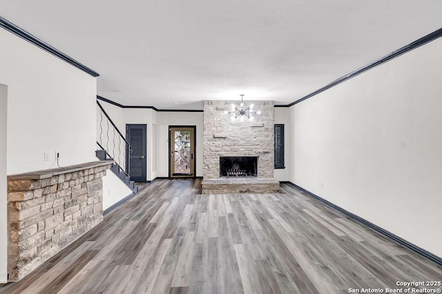 unfurnished living room featuring wood-type flooring, crown molding, a stone fireplace, and an inviting chandelier