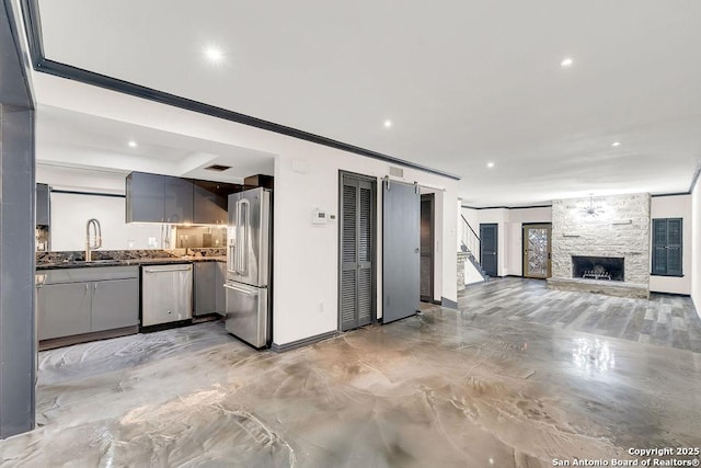 kitchen featuring stainless steel appliances, a stone fireplace, sink, gray cabinetry, and crown molding