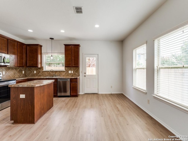 kitchen featuring a kitchen island, stainless steel appliances, light hardwood / wood-style floors, sink, and hanging light fixtures