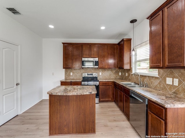 kitchen featuring light hardwood / wood-style floors, appliances with stainless steel finishes, a center island, decorative light fixtures, and sink