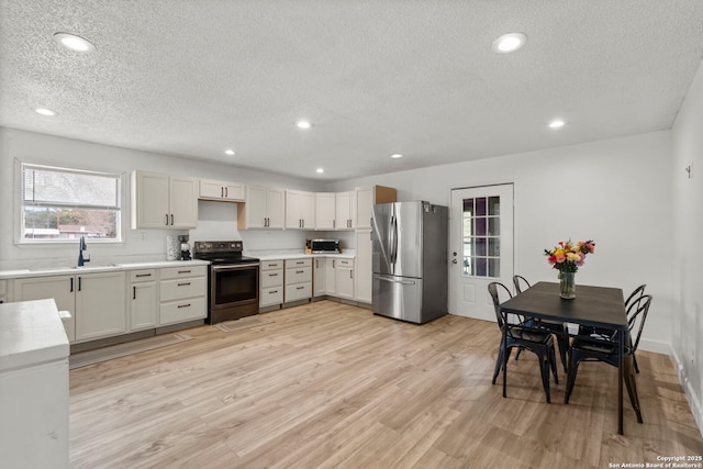 kitchen with light wood-type flooring, appliances with stainless steel finishes, a textured ceiling, and sink