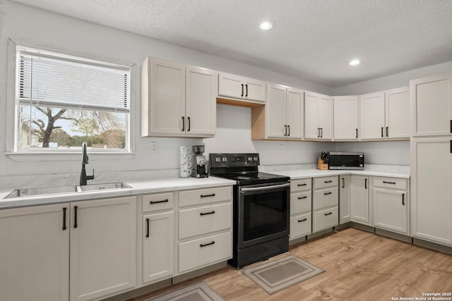 kitchen with a textured ceiling, appliances with stainless steel finishes, white cabinetry, light hardwood / wood-style floors, and sink