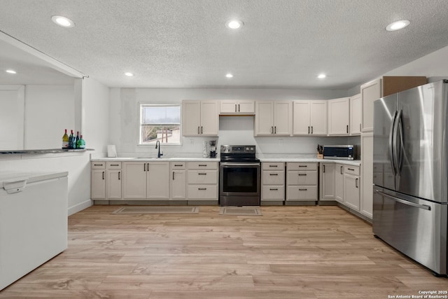 kitchen with white cabinetry, a textured ceiling, stainless steel appliances, and light wood-type flooring