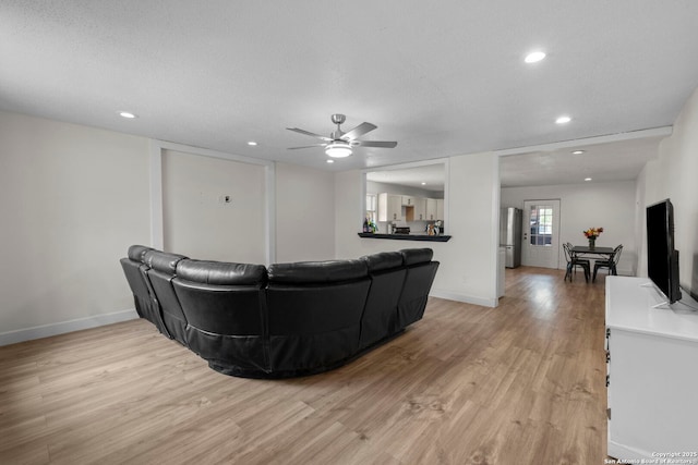 living room featuring ceiling fan, a textured ceiling, and light hardwood / wood-style flooring