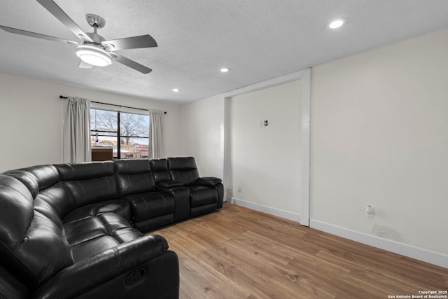 living room with a textured ceiling, ceiling fan, and light hardwood / wood-style flooring