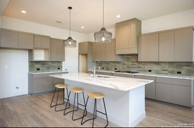 kitchen with an island with sink, sink, gray cabinets, light wood-type flooring, and stainless steel gas stovetop