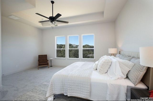 carpeted bedroom featuring ceiling fan and a raised ceiling