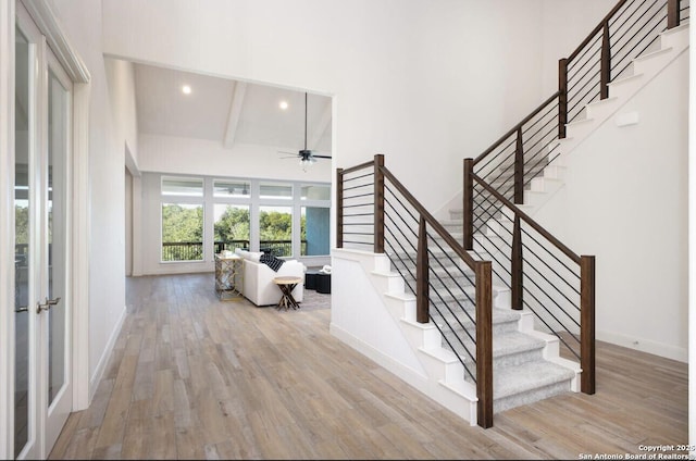 stairway with hardwood / wood-style flooring, ceiling fan, beamed ceiling, and a towering ceiling