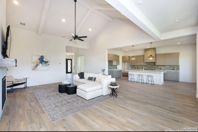 living room with light wood-type flooring, ceiling fan, beamed ceiling, and high vaulted ceiling