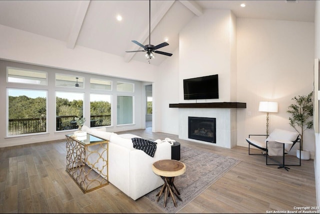 living room featuring high vaulted ceiling, hardwood / wood-style floors, a tile fireplace, and beam ceiling