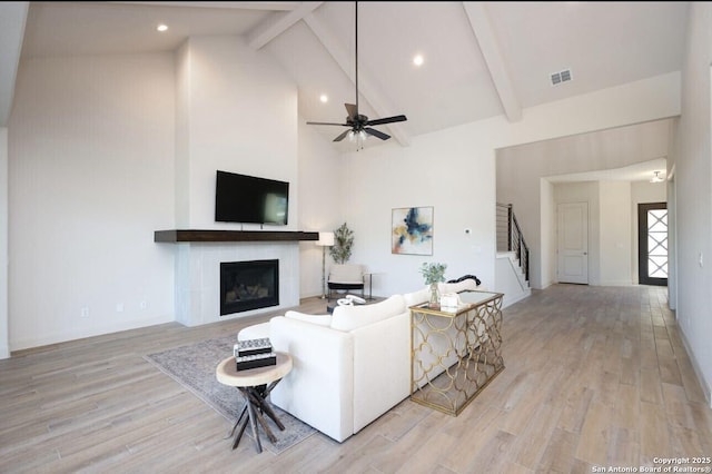 living room featuring beam ceiling, a tiled fireplace, high vaulted ceiling, and light hardwood / wood-style floors