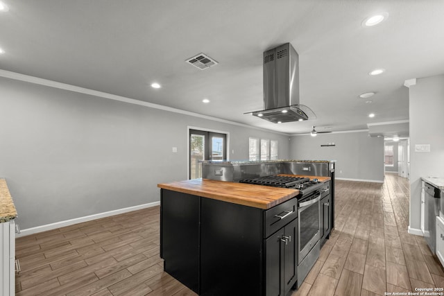 kitchen featuring a center island, wood counters, island range hood, stainless steel gas range oven, and ceiling fan