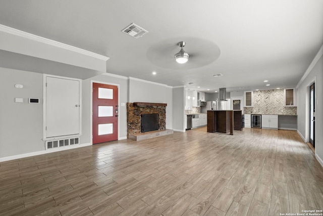 unfurnished living room featuring hardwood / wood-style flooring, ceiling fan, a fireplace, wine cooler, and crown molding