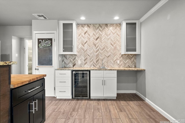 kitchen with white cabinetry, wine cooler, light stone counters, and sink