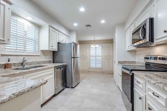 kitchen featuring white cabinets, appliances with stainless steel finishes, decorative light fixtures, sink, and light stone counters